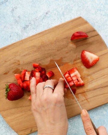 two hands chopping strawberries.