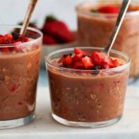 two glass jars with brown oats topped with chopped strawberries.