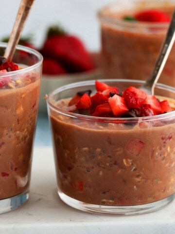 two glass jars with brown oats topped with chopped strawberries.