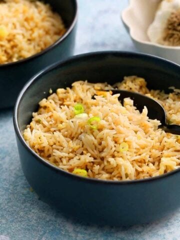 cooked garlic fried rice in two blue bowls along with a black spoon.