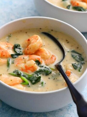 shrimp and spinach soup in a white bowl along with a black spoon.