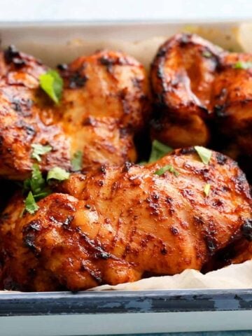 cooked orange chicken thighs in a white platter garnished with green cilantro.