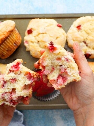 two hands holding two halves of a strawberry muffin.