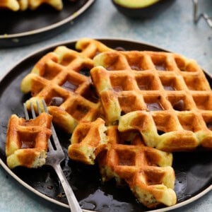 three avocado waffles placed on a round black plate along with a fork.