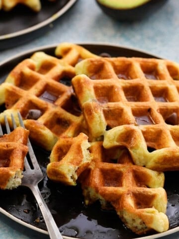 three avocado waffles placed on a round black plate along with a fork.