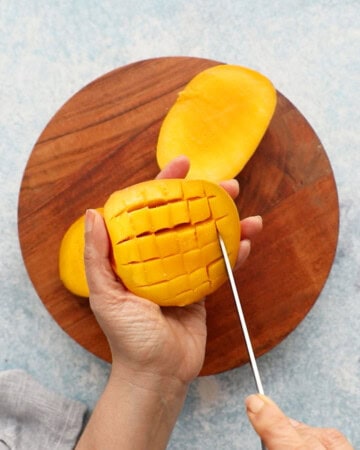 two hands cutting one mango half into dice.