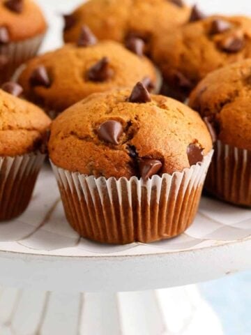 7 pumpkin chocolate chip muffins placed on a white cake stand.