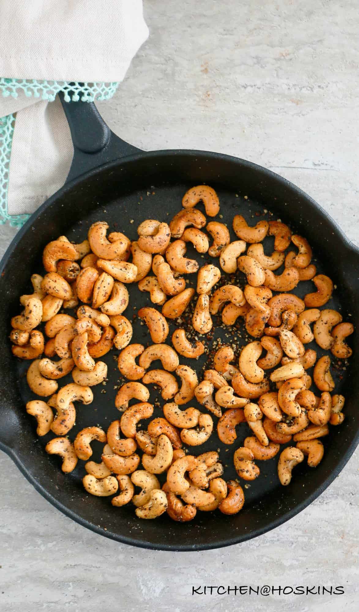 SALT AND PEPPER CASHEWS in a cast iron skillet with handle wrapped in a kitchen linen