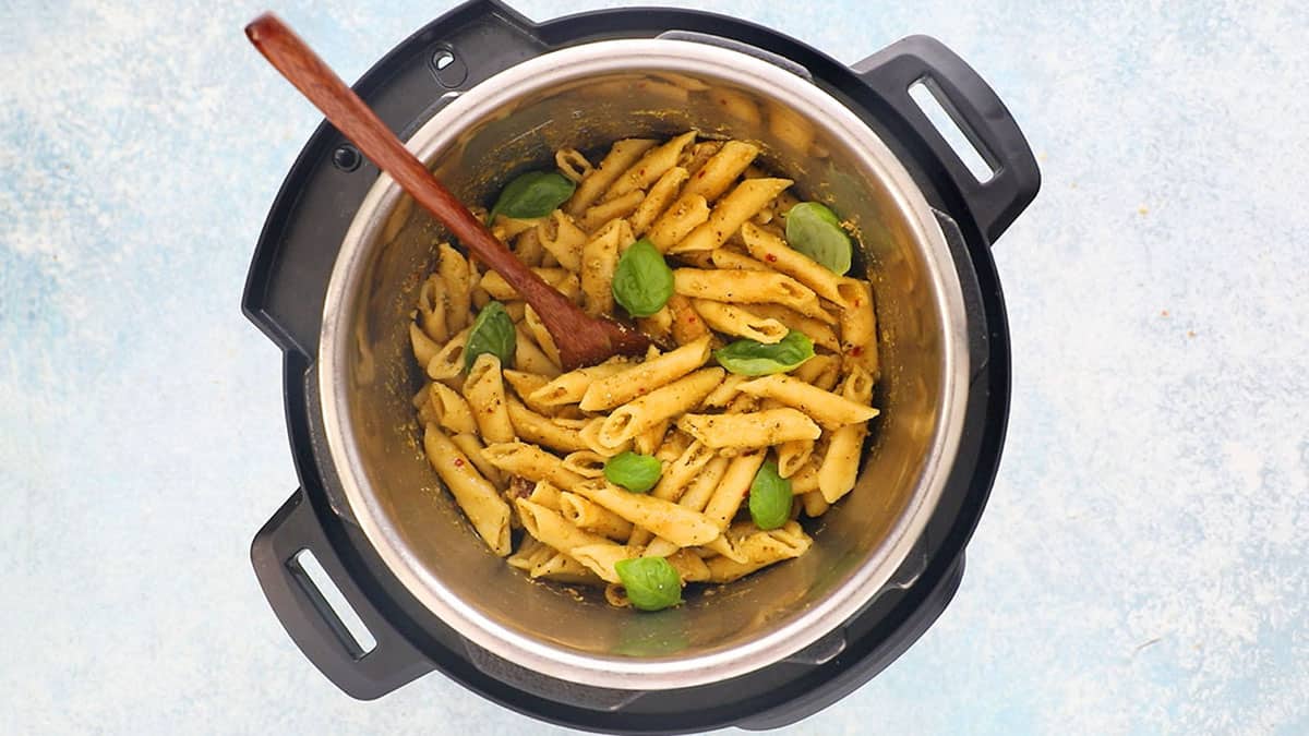 cooked penne pesto pasta garnished with green basil leaves in an instant pot.