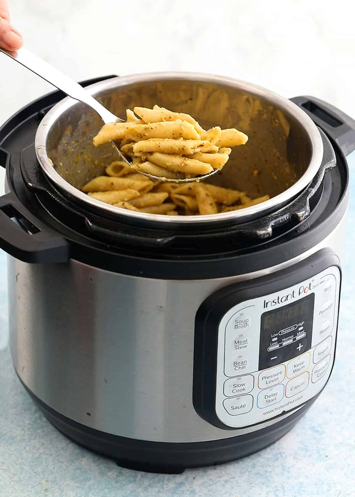 a hand lifting a ladle full of cooked penne pasta from an instant pot.