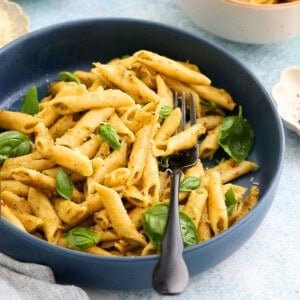 cooked pesto penne pasta along with a black fork in a large blue bowl.
