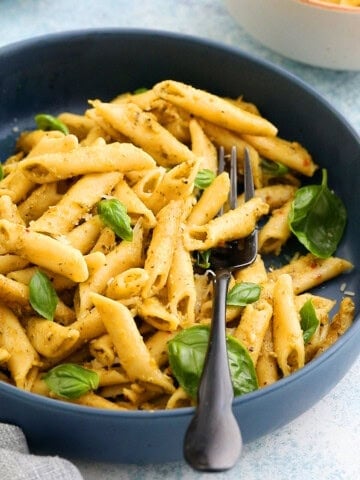 cooked pesto penne pasta along with a black fork in a large blue bowl.