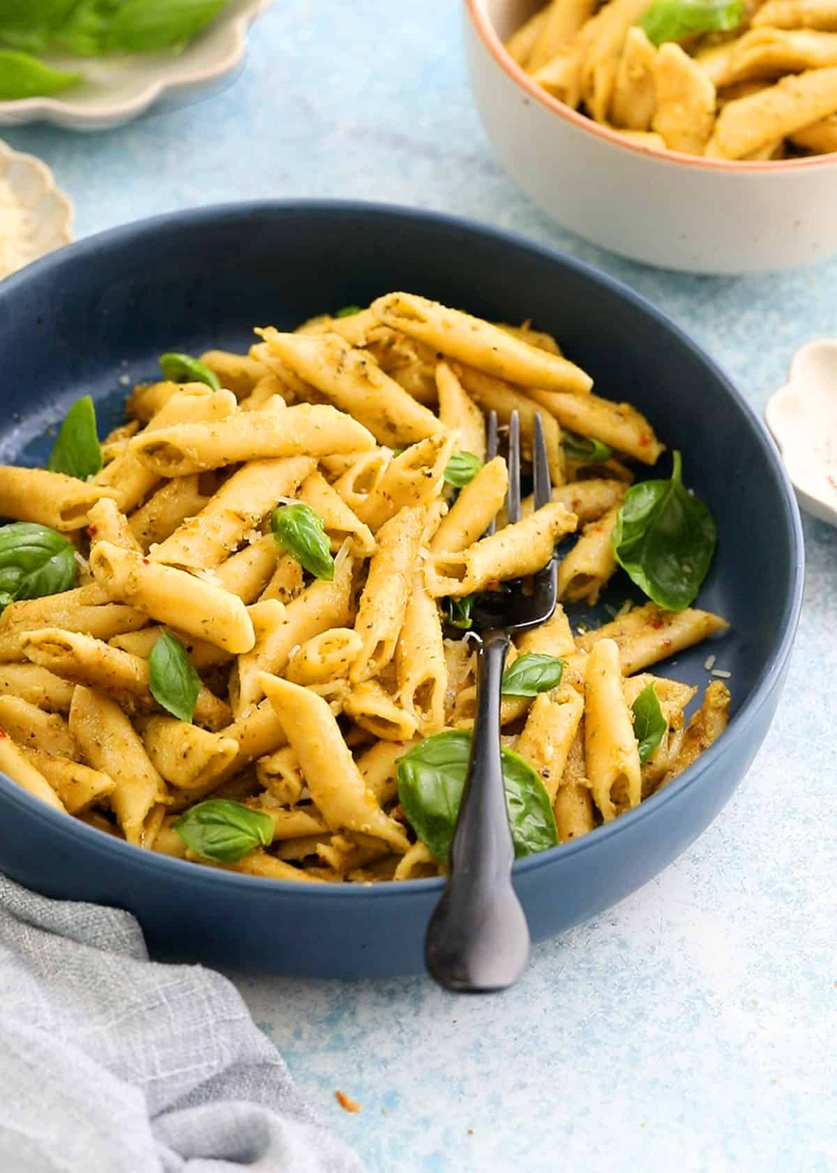 cooked penne pesto pasta in a large blue bowl along with a black fork.