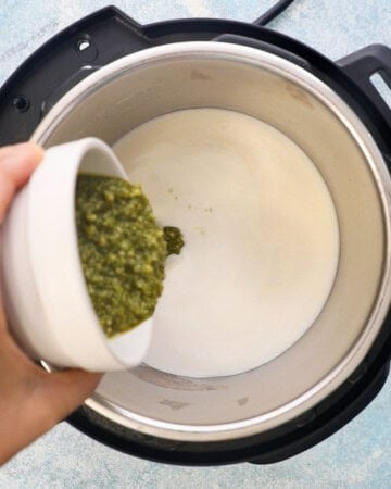 a hand adding green pesto sauce into an instant pot. 