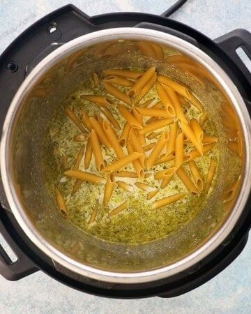 raw penne pasta along with green liquid in an instant pot.