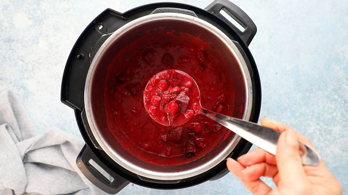 a hand holding a ladle full of pink beet curry above an instant pot.
