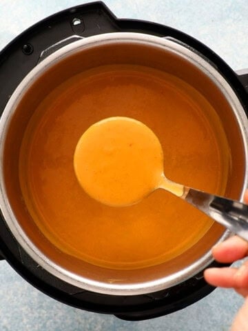 a hand holding one ladle full of orange colored cauliflower soup.