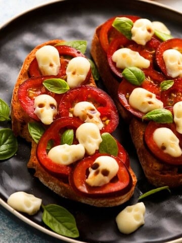 two tomato toasts topped with white skulls in a black plate.