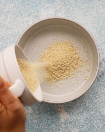 a hand pouring panko bread crumbs into white shallow dish.