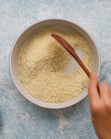 a hand mixing white breadcrumbs in a white round dish.