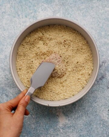 a hand coating one raw chicken piece in panko breadcrumbs.