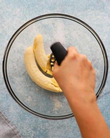 a hand mashing two bananas using a potato masher.