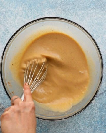 a hand whisking brown liquid in a large glass bowl.