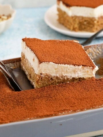 a hand removing one slice of tres leches cake from a baking pan.