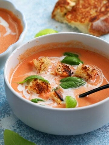 pink colored tomato soup topped with green basil in a white bowl.