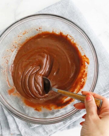 a hand stirring melted chocolate in a glass bowl using a spoon.