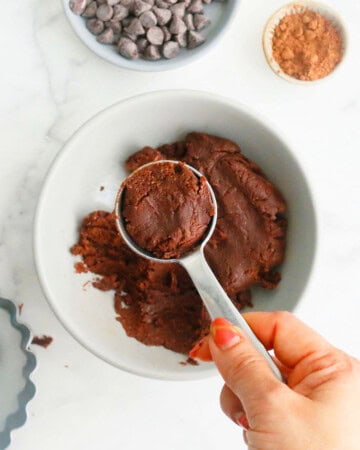 a hand holding one tablespoon filled with brown chocolate dough.