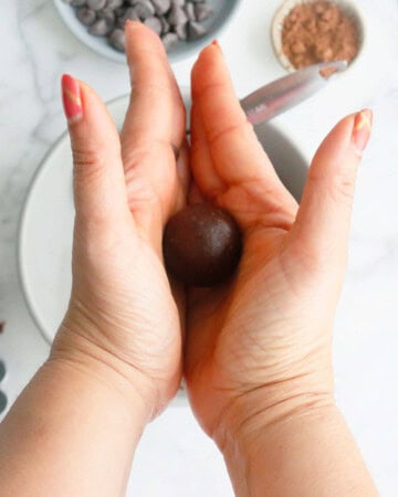 two hands rolling one brown chocolate ball.