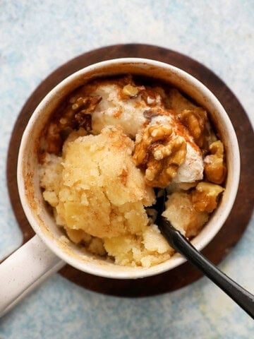 cooked apple cake in a white mug along with a black spoon.