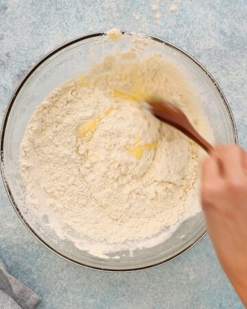 two hands mixing muffin batter in a glass bowl.