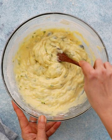two hands mixing muffin batter in a large glass bowl.