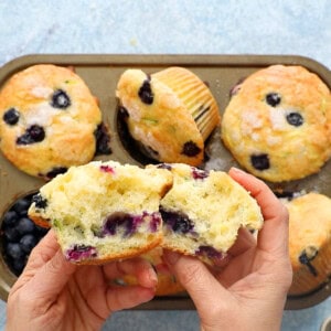 two hands holding two split halves of a blueberry muffin.