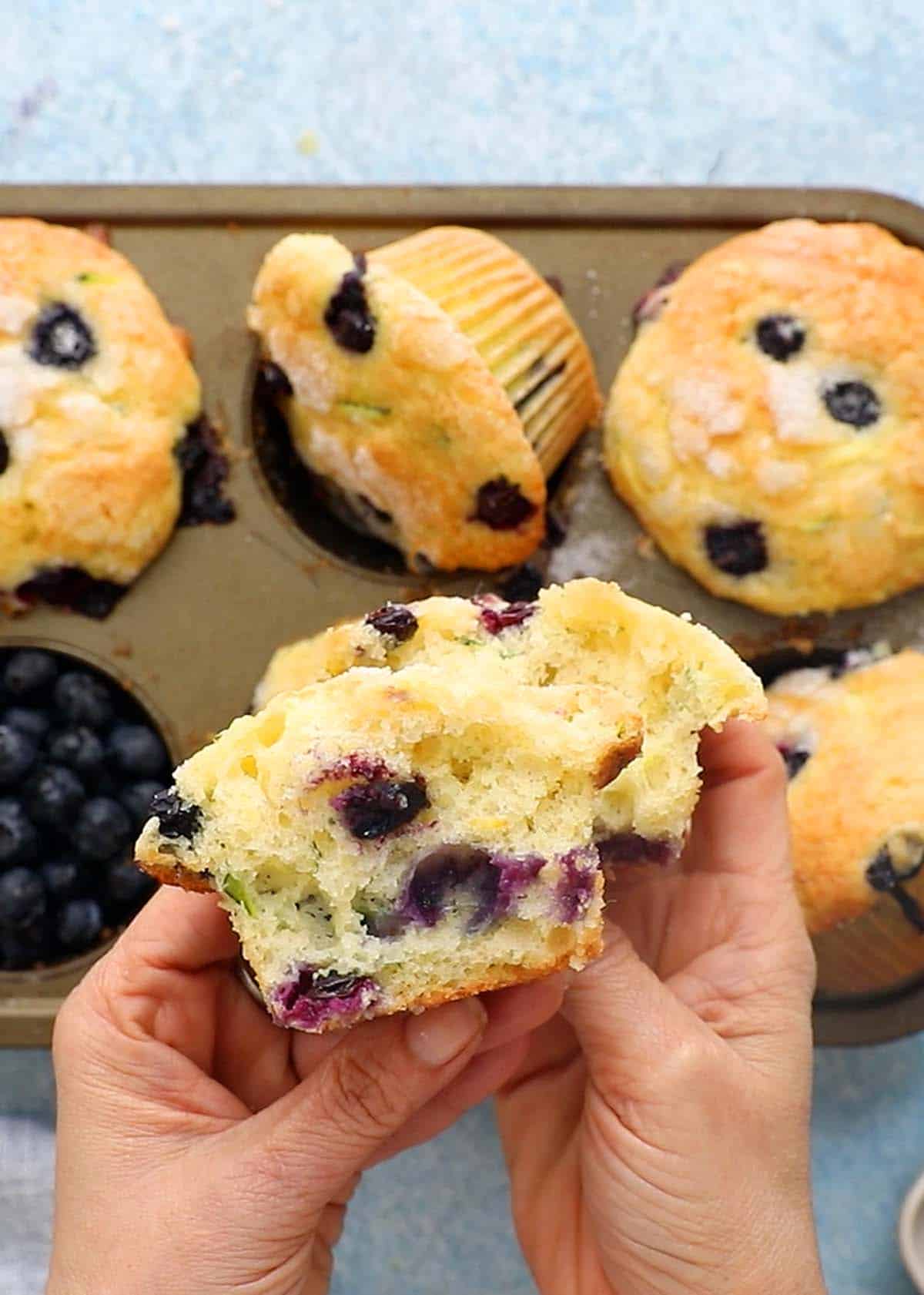 two hands holding two halves of a blueberry muffin.