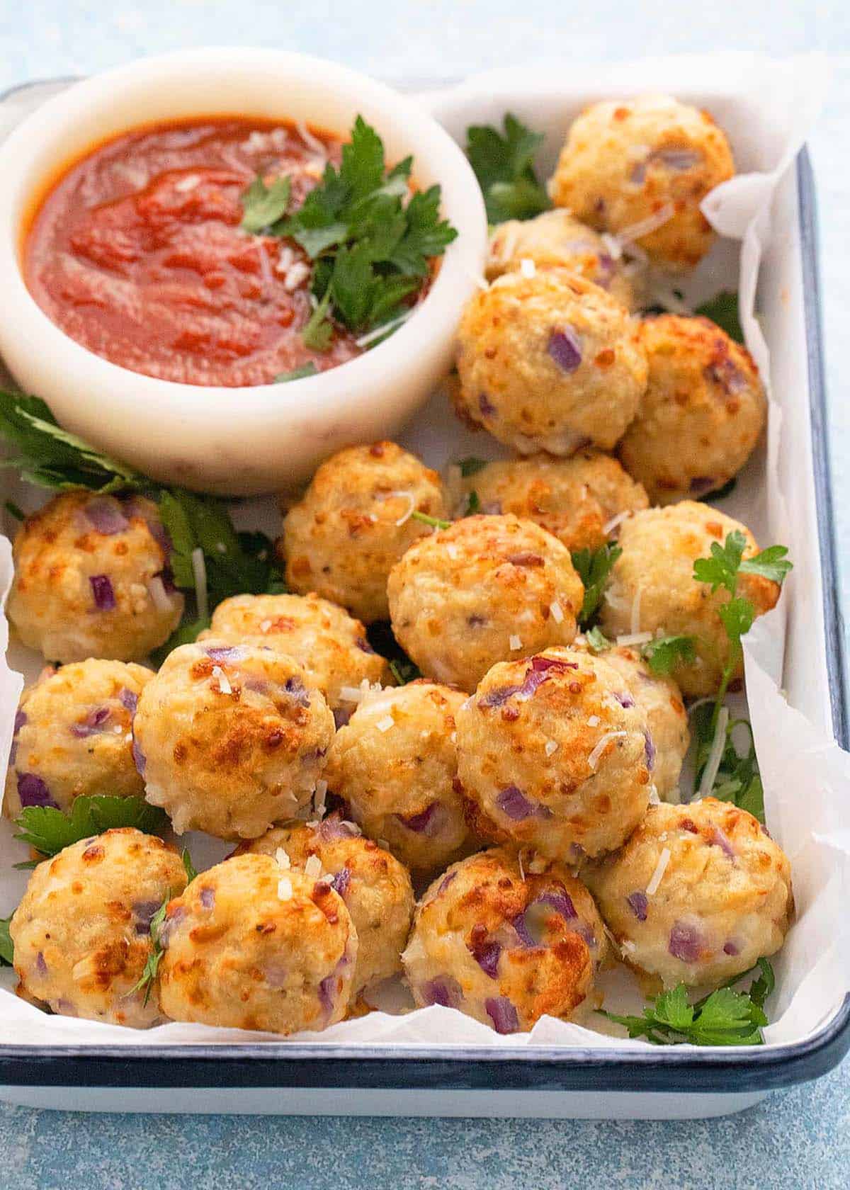 cooked chicken meatballs placed in a white tray along with a white bowl with red marinara sauce.
