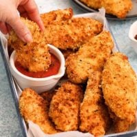 a hand dipping one breaded chicken tender in tomato sauce.
