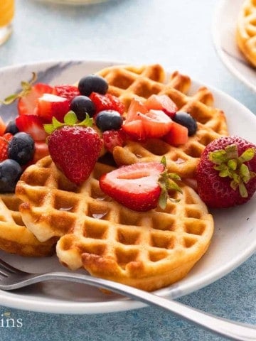 mini waffles on a white plate topped with berries and syrup.