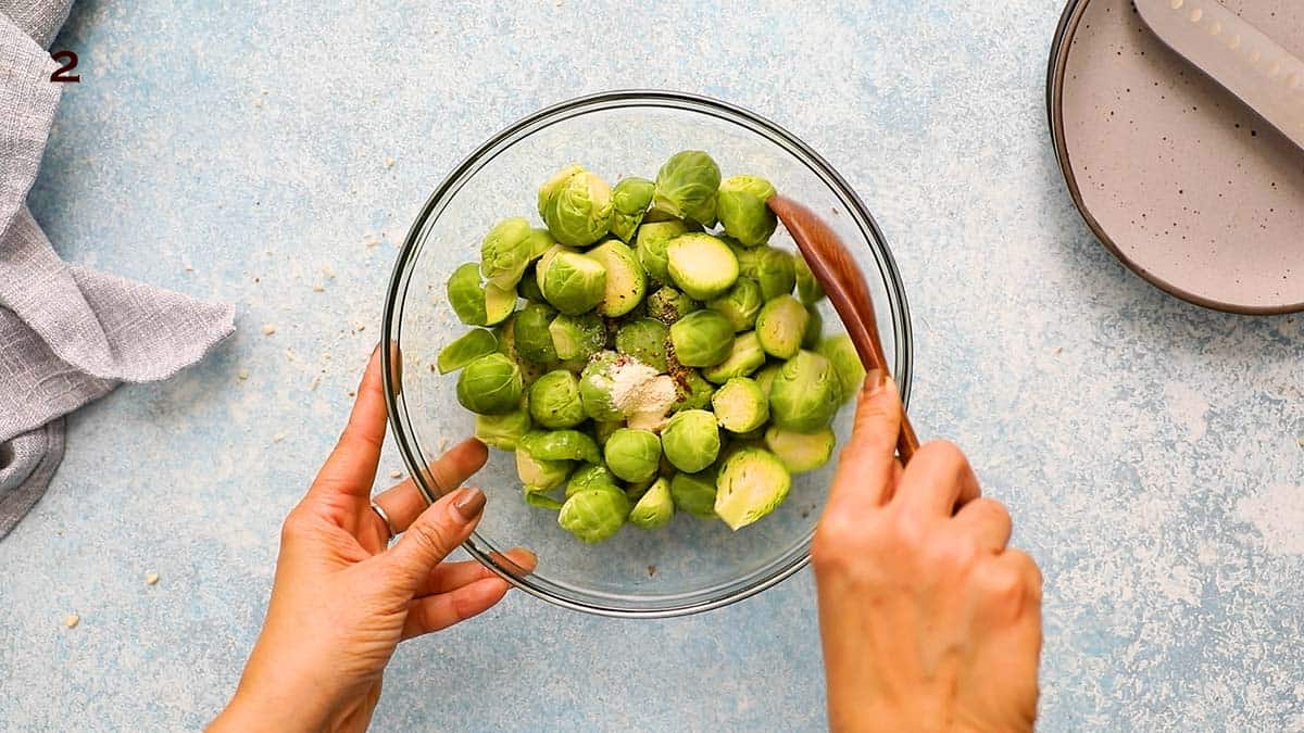 two hands mixing brussels sprouts in a glass bowl.