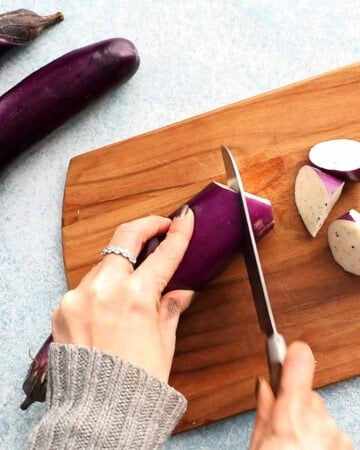two hands cutting an eggplant into chunks.