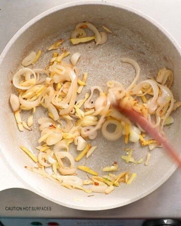 a hand cooking sliced shallots in a white skillet.