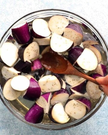 a hand pressing eggplant chunks into a bowl of glass bowl.