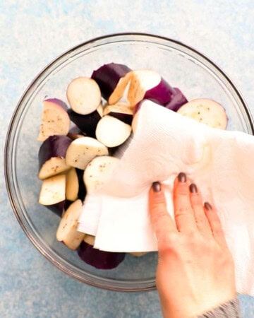 a hand patting dry eggplant chunks using a white paper towel.