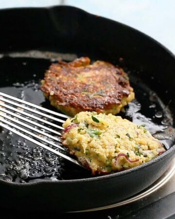 three zucchini fritters cooking in a black skillet.