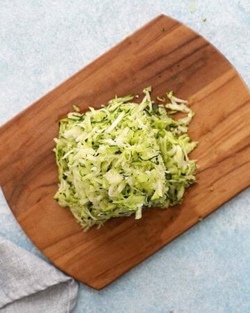 grated zucchini piled on a wooden board.