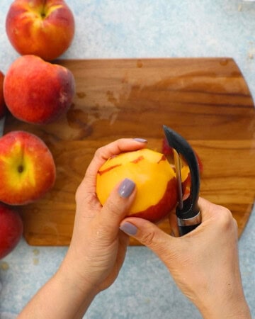two hand peeling the skin of a peach using a black peeler.