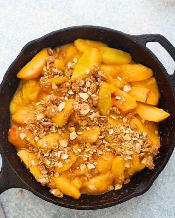 sliced peaches topped with oats and almonds in a black skillet.
