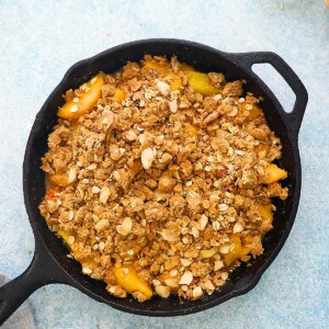 sliced yellow peaches topped with crumble topping in a black skillet.